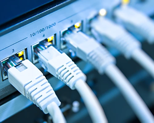 Nahaufnahme eines Netzwerk-Switches mit mehreren angeschlossenen weißen Ethernet-Kabeln und leuchtenden Statusanzeigen an den Gigabit-LAN-Ports. Symbolbild für kabelgebundene Netzwerke, LAN und professionelle Netzwerktechnik.
