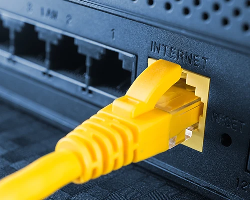 Gelbes Ethernet-Netzwerkkabel steckt im gekennzeichneten Internet-Port eines Routers; daneben befinden sich mehrere freie LAN-Anschlüsse und die Reset-Taste. Symbolbild für Router-Konfiguration, Internetanschluss und Netzwerk-Support.