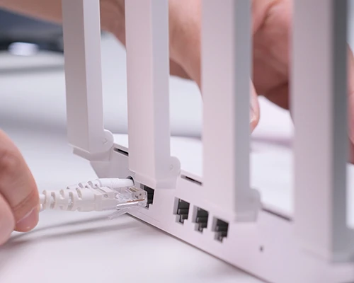 Nahaufnahme eines weißen WLAN-Routers mit mehreren Antennen: Eine Hand verbindet ein weißes Ethernet-Kabel mit einem Netzwerkanschluss auf der Rückseite. Symbolbild für WLAN-Einrichtung, Router-Konfiguration und Heim- oder Büronetzwerke.